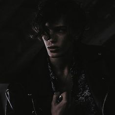 a young man wearing a black leather jacket in the dark with his hand on his chest