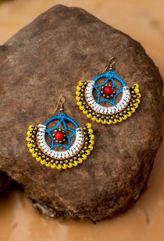 two pairs of earrings sitting on top of a rock next to a rock with an orange and yellow beaded design