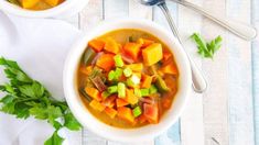 two bowls filled with soup on top of a white wooden table next to spoons