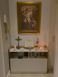 a white shelf with candles and pictures on it in front of a painting hanging on the wall