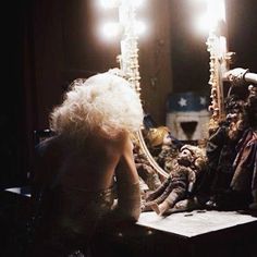 a woman sitting in front of a mirror next to a man with long white hair