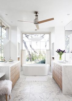 a white bathroom with marble flooring and large windows overlooking the trees in the distance