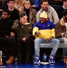 two people sitting on a bench at a basketball game, one is wearing a yellow hat and the other has blue shoes