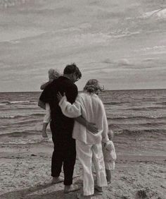 an older man and two younger women walking on the beach with their arms around each other