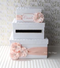 three white boxes with pink flowers and ribbons on the top one has a name card in it