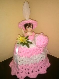 a doll sitting on top of a crocheted chair with a flower in it