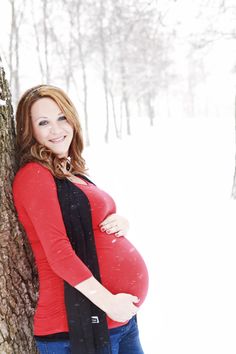 a pregnant woman leaning against a tree in the snow