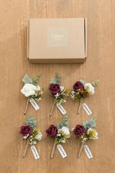 six boutonnieres with flowers and greenery on a table next to a box