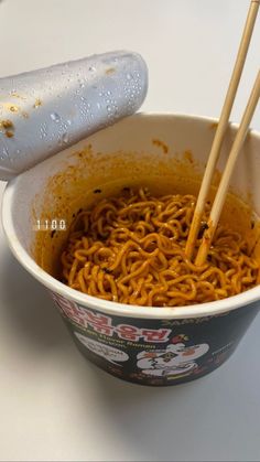 a bowl of noodles with chopsticks sticking out of it, on a table