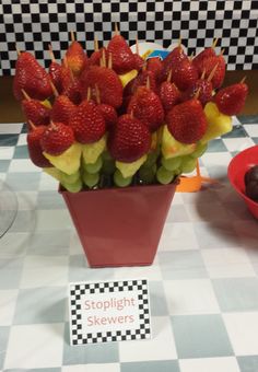 strawberries and grapes are arranged in a vase on a checkered tablecloth with a sign that says stoplight skewers