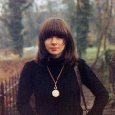 a woman standing in front of a fence with her hands on her hips and wearing a black sweater