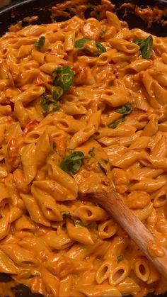 macaroni and cheese is being cooked in a skillet with a wooden spoon