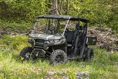 a can - am defender off road vehicle parked in the grass with trees behind it