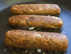 three sausages cooking in a frying pan