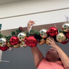 a woman is hanging ornaments from the ceiling in front of christmas decorations on a pole