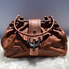 - Beautiful Tan/Camel Soft Calfskin Leather - Silver Buckle Clasp Closure With Three Adjustable Buckle Holes - Double Leather Handles (7” Drop) - Brown Fabric Lining With Large Leather Pull Zipper Compartment Inside - Silver Tone Hardware - Four Studs To Protect Bottom - Measurement: 9” H X 12.5” L X 4.25” D - P.S. Light Mark/Scratches/Wrinkles/Dark On Soft Leather, Light Scratches On Silver Hardware (Please See All Photos As Part Of Description) - Made In Italy - Pre-Loved, In Great Condition, Besides P.S. Part Tods Bag, Brown Fabric, Leather Shops, Leather Pulls, Leather Silver, Shoulder Handbag, Leather Handles, Silver Hardware, Leather Handle