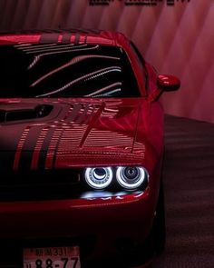 the front end of a red sports car with its lights turned on and it's hood up