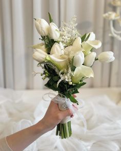 a bouquet of white tulips and lilies in someone's hand on a bed