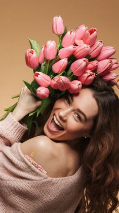 a woman is smiling and holding a bunch of pink tulips on her head