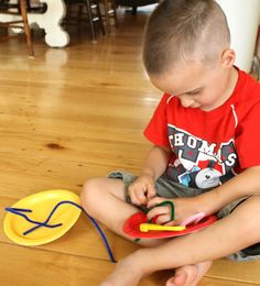 a young boy sitting on the floor playing with his construction toys and cutting paper scissors