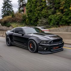 a black car driving down the road with trees in the background