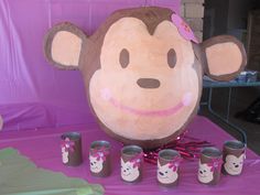 there is a stuffed monkey with many cups in front of it on a purple table cloth