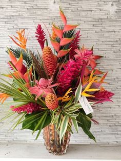 a vase filled with lots of colorful flowers on top of a white table next to a brick wall