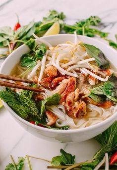 a white bowl filled with noodle soup and vegetables on top of a marble counter