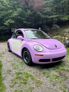 a purple and white beetle parked on top of a gravel road in front of trees