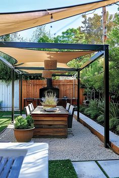 Outdoor dining area with a wooden table, chairs, plants, and a shade canopy. The background features a fence, greenery, and a fireplace. Shaded Outdoor Sitting Area, Backyard Sun Shade Ideas, Shaded Patio Ideas, Backyard Shade Ideas On A Budget, Shade Cloth Ideas Patio, Outdoor Shade Ideas, Backyard Shade Ideas