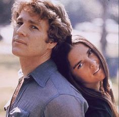 a man and woman standing next to each other in front of a park with trees