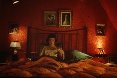 a woman sitting on top of a bed reading a book in a red lit room