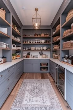 a large kitchen with gray cabinets and white rugs on the hardwood floor, along with shelves filled with dishes