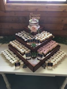 a table topped with lots of cupcakes covered in frosting next to a window