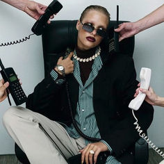 a woman sitting in a chair while talking on the phone and two hands holding phones