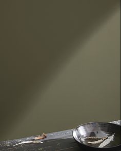 a metal bowl sitting on top of a wooden table next to a green painted wall