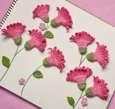 pink crocheted flowers are on a white notebook with green leaves and stems in the middle