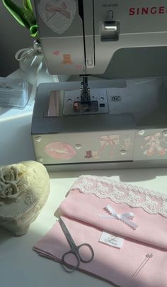 the sewing machine is sitting next to some pink cloths and a white vase with flowers