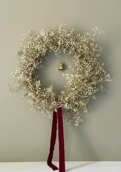 a christmas wreath hanging on the wall with a red ribbon around it and a bell in the middle