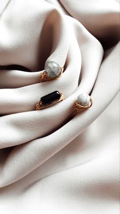 two rings are sitting on top of a white cloth with black and white stones in the middle