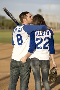 a man and woman embracing each other on a baseball field with bats in their hands