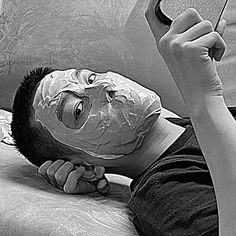 a man laying on top of a bed with a sheet covering his face and holding a cell phone