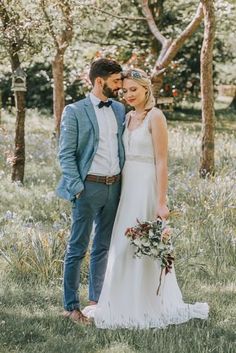 a bride and groom are standing in the grass near some trees with their bouquets