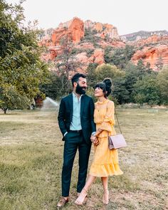 a man and woman standing next to each other in a field with mountains behind them