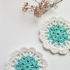 two crocheted coasters sitting on top of a table next to a vase with flowers