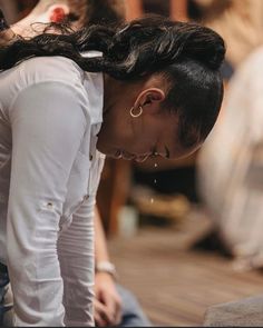 a woman sitting on the ground with her head down and ear piercings in her ears