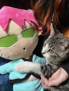 a cat that is laying down next to a stuffed animal and a person with red hair