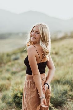 a woman standing on top of a grass covered field wearing a black tank top and tan pants