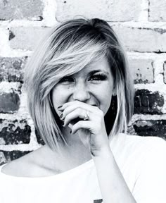 a black and white photo of a woman holding her hand to her mouth, smiling