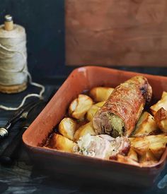 a dish filled with potatoes and meat next to a spool of thread on a table